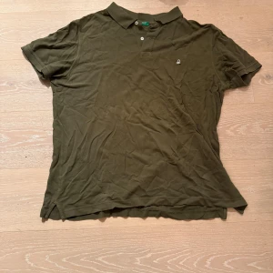 Olivgrön pikétröja Benetton XXL - Olivgrön pikétröja från United Colors of Benetton i storlek XXL. Klassisk krage, korta ärmar och två knappar framtill. Diskret broderad logga på bröstet. Tröjan är gjord i mjuk bomull och har en clean, enkel look som funkar till jeans eller shorts.