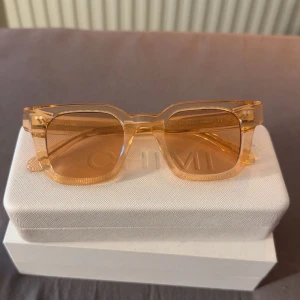 CHIMI ljusorange fyrkantiga solglasögon - Snygga solglasögon från CHIMI i en transparent ljusorange färg. Modellen har en fyrkantig form och tjock båge som ger en cool retrovibe. Perfekta för dig som vill sticka ut med stilrena accessoarer. Levereras med glasögonfodralet men ej boxen.