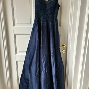 Marinblå balklänning  - Säljer min marinblåa balklänning som är superfin. Endast använd en gång! Den har fina detaljer och är i väldigt bra kvalitet. Fickor och dragkedja i ryggen samt 3 lager på kjolen. Storlek 32 från JJ House. Lite uppsydd och är lite för lång för mig som är 155 så passar perfekt med ett par klackar. Skriv för fler bilder!!