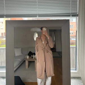 Beige trenchcoat från Bik Bok - Snygg beige trenchcoat från Bik Bok i storlek M. Jackan har klassisk krage, knytskärp i midjan och praktiska fickor. Materialet är mjukt och har ett snyggt fall, perfekt för dig som gillar stilrena och chill plagg. Passar dig som vill ha en clean look.
