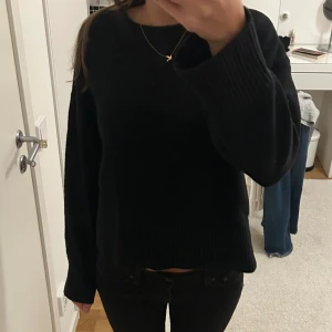 Svart stickad tröja med breda ärmar - Säljer en svart stickad tröja med breda, långa ärmar och rund hals. Tröjan har en enkel och clean look med ribbade muddar vid ärmslut och nederkant. Perfekt för dig som gillar minimalistisk stil och vill ha något mjukt och bekvämt.