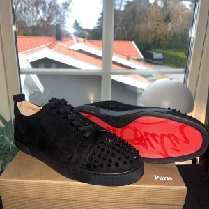 Christian Louboutin svarta sneakers - Svarta sneakers från Christian Louboutin med ikonisk röd sula och svarta spickar på tån. Skorna har snörning och är tillverkade i mocka med läderfoder. Snygg och edgy design som sticker ut med sina detaljer och exklusiva känsla. Använda max 15 gånger med ett sulskydd 