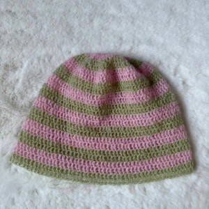 Randig virkad mössa i rosa och grön - Säljer en mysig virkad randig mössa i ljusrosa och ljusgrönt. Mössan har en klassisk form och är virkad i ett alpacka garn som är mjukt och sticks inte. Perfekt för dig som gillar färg och vill ha en chill accessoar till hösten och vintern.