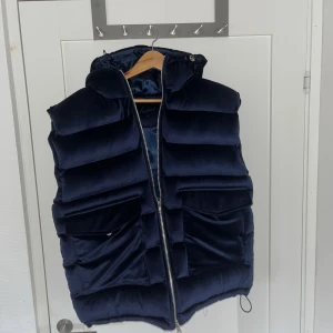 Väst från Vendiera - Snygg mörkblå dunväst från Vendiera med fluffig, quiltad design och stor huva. Västen har två stora fickor framtill och dragkedja hela vägen. Materialet är mjukt och har en lyxig känsla, perfekt för att hålla värmen under kyliga dagar