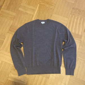Grå stickad tröja från Sandö - En stilren grå stickad tröja från Sandö i storlek S. Tröjan har rund halsringning, ribbade muddar och är långärmad. Perfekt för lager-på-lager och enkel att matcha med jeans eller chinos.