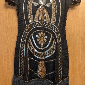 Gatsby-klänning. Svart paljettklänning. - Kort Gatsby-klänning med fransar och paljetter. Aldrig använd. Köpt till en fest som aldrig blev av.