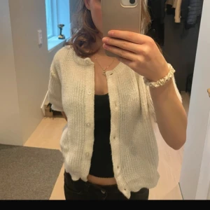 Vit stickad kofta med kort ärm💕💕 - Superfin vit stickad kofta med korta ärmar och rund hals. Koftan har ribbade muddar och knäpps med vita knappar framtill. Perfekt att slänga över ett linne eller t-shirt för en chill och stilren look.