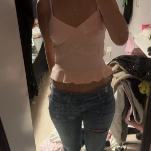 Ljusrosa volang linnetopp - Säljer en ljusrosa linnetopp med volangdetaljer och v-ringad hals. Toppen är croppad och har smala axelband, perfekt för sommarens alla häng. Materialet känns lätt och luftigt, och volangen ger en söt och feminin touch.