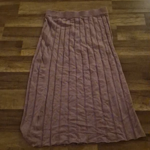 Ljuslila långkjol från Stories - Säljer en ljuslila långkjol från Stories i storlek S. Kjolen har ett ribbat midjeband och vertikala ribbade ränder som ger en snygg struktur. Materialet känns mjukt och stretchigt, perfekt för dig som gillar bekväma och stilrena plagg.