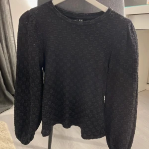 Svart blommig blus från H&M - Supersnygg svart blus från H&M i storlek XS med diskret blommigt mönster. Blusen har långärmade puffärmar med resår vid ärmslut och rund halsringning. Materialet är mjukt och har en lätt struktur som ger en cool vibe.
