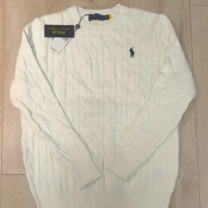 Vit kabelstickad tröja Polo Ralph Lauren - Kabelstickad Ralph Lauren tröja i vit med den klassiska Polo-loggan på bröstet. Tillverkad i 100% mjuk bomull som sitter bekvämt och håller formen fint. 📏Storlek M, längd 65 cm och bredd 48,5 cm. Oanvänd i fint skick. Meddela för frågor!