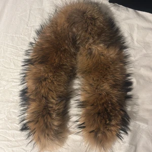Päls - Supermjuk päls i ljusbrun med mörka toppar. kan sättas på vinterjackor eller en vanlig jacka pga två spännen längst ner. Fodrad med svart tyg på insidan för extra komfort. Perfekt accessoar för att lyfta vinterlooken.