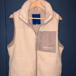 Beige fleeceväst  - Säljer en beige fleeceväst från jack&jones med hög krage och dragkedja framtill. Västen har en ljusgrå bröstficka med dragkedja och tryckt logga, samt två sidofickor. Perfekt för lager-på-lager och