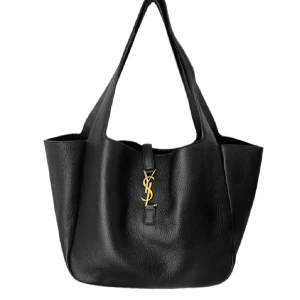 Svart axelväska från Saint Laurent - Snygg svart axelväska från Saint Laurent i mjukt, strukturerat skinn med guldigt YSL-emblem framtill. Väskan har rymligt huvudfack, innerficka med dragkedja och stilrena handtag. Perfekt för dig som vill ha en lyxig och klassisk look.