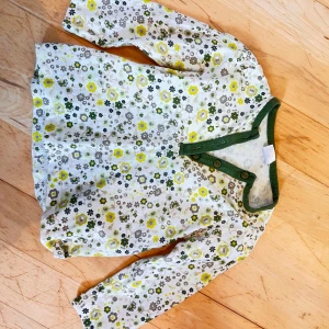 Blommig långärmad tröja Zara Baby - Söt långärmad tröja från Zara Baby med blommigt mönster i grönt, gult och beige på vit botten. Tröjan har gröna kantband och knappar vid halsen för enkel påklädning. Perfekt för vår och sommar!