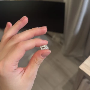 Silvriga örhängen med glittriga stenar - Säljer ett par stilrena silvriga örhängen i klassisk bågform, dekorerade med gnistrande stenar längs framsidan. Perfekta för dig som gillar en elegant och tidlös look med lite extra bling.