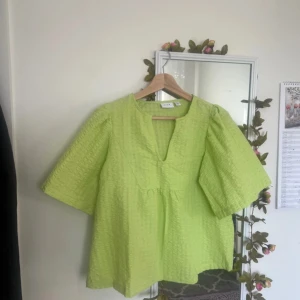 Ljusgrön blus från Nelly - Säljer en ljusgrön blus från Nelly med puffiga, korta ärmar och v-ringad hals. Blusen har en strukturerad, quiltad yta och är lätt och luftig i modellen. Perfekt för dig som gillar färg och vill sticka ut lite extra.