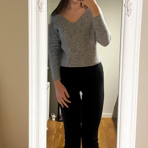 Grå ribbad stickad tröja med v-ringning - Säljer en grå stickad tröja med snygg v-ringning och ribbad struktur. Modellen är croppad och har långa ärmar, perfekt för lager-på-lager. Enkel att matcha med både jeans och kjol för en chill look.