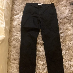 Svarta chinos från These Glory Days - Svarta chinos från These Glory Days Scandinavia med klassisk rak passform och bälteshällor. Snygga detaljer med bakficka och stilren design. Perfekta för dig som gillar enkel och clean stil.