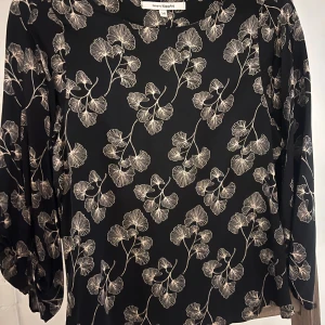 Svart blus med blommigt mönster KappAhl - Snygg svart blus från KappAhl med beige blommigt mönster. Blusen har rund halsringning och långa ärmar med lätt puff vid axlarna. Perfekt för dig som gillar stilrena och trendiga prints. Materialet känns mjukt och följsamt mot huden.