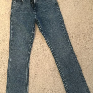 Blå jeans från Tommy Hilfiger - Snygga blå jeans från Tommy Hilfiger med klassisk femficksdesign och raka ben. Jeansen har hög midja, tydliga sömmar och logotypdetaljer på ficka och bakre läderpatch. Tillverkade i bomull med en cool tvättad finish.