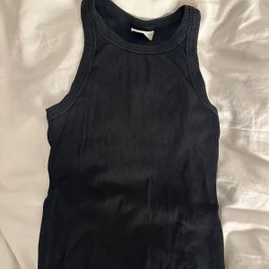 Svart ribbad linnetopp från Gina Tricot - Svart ribbad linnetopp från Gina Tricot, modellen Basically Basket. Toppen är ärmlös med rundad hals och har en tight passform. Perfekt att styla med jeans eller kjol för en clean och enkel look.