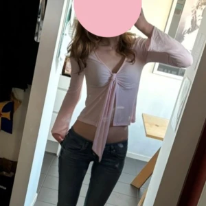 Ljusrosa omlottopp med knyt - Säljer en ljusrosa topp med långa ärmar och djup v-ringning. Toppen har en snygg knyt-detalj framtill som ger en trendig look. Perfekt att styla med jeans eller kjol för en cool outfit.