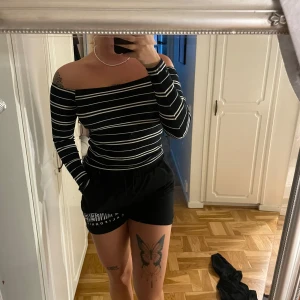 Randig offshoulder topp från Bik Bok - Säljer en svart och vit randig offshoulder topp från Bik Bok i ribbad bomullsmix. Toppen har långa ärmar och sitter tight mot kroppen, perfekt för dig som gillar en stilren men ändå trendig look.