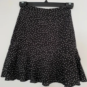 Svart prickig kjol från SHEIN XS - Supersöt svart kjol från SHEIN med vita prickar och volang nedtill. Kjolen har en kort och lätt utsvängd form som ger en skön vibe. Storlek XS, EU 34.