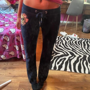 Juicy Couture mörkblå mjukisbyxor - Mörkblå mjukisbyxor från Juicy Couture i mjuk sammet med broderat JC-logga och blommor i guld, rosa och vitt på ena benet. Byxorna har snörning i midjan och vida ben. Perfekta för en chill och snygg look. Storleken är S men skulle säga att den är mer åt xs/xss hållet 