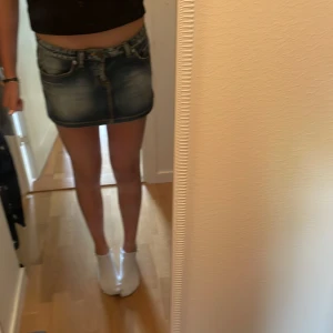 Blå jeanskjol från Phard - Storleken är 28 men passar för S och M .Snygg kort jeanskjol från Phard med klassisk femficksdesign, slitna detaljer och ljusblå tvätt. Kjolen har knapp och dragkedja framtill samt bälteshällor. Perfekt för dig som hillar korta kjolar med true religion fickor 