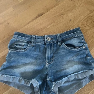 Blå jeansshorts från LAB Industries - Snygga blå jeansshorts från LAB Industries med fransad kant och klassisk femficksdesign. Shortsen har knapp och dragkedja framtill, bälteshällor och slitna detaljer för en cool look. Perfekta för varma dagar och chill stil.