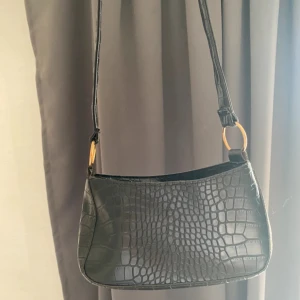 Svart axelväska  - Snygg svart axelväska med guldfärgade ringdetaljer vid axelremmen. 