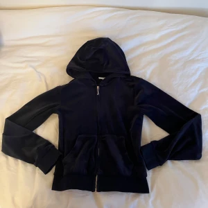 Mörkblå velour hoodie Juicy Couture - Snygg mörkblå hoodie från Juicy Couture i mjuk velour med broderad JC-logga på bröstet. Tröjan har huva, dragkedja framtill och två fickor. 