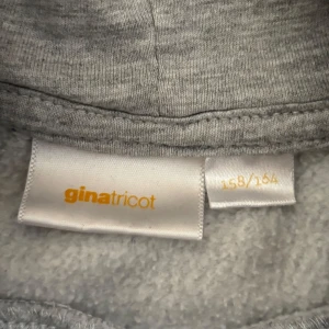 Grå hoodie med tryck från Gina Tricot - Säljer en grå hoodie från Gina Tricot med svart texttryck 'JE M'EN AMOUR' och en stjärna på både bröstet och ryggen. Säljer för ja använder inte, pris kan diskuteras 🩷