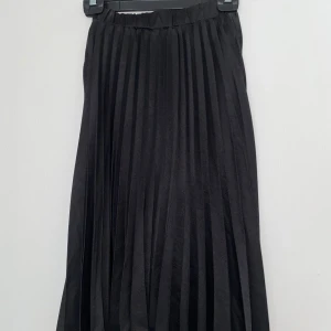Svart plisserad långkjol från SHEIN - Svart plisserad långkjol från SHEIN i storlek S. Kjolen har ett elastiskt midjeband och snygga, djupa veck som ger ett flowy och trendigt uttryck. Perfekt för dig som gillar stilrena och klassiska plagg med lite edge.