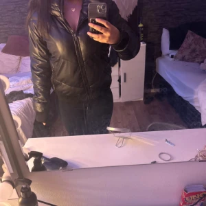 Svart pufferjacka med huva - Säljer en svart pufferjacka med huva och dragkedja framtill. Jackan har en lite glansig yta och breda muddar vid ärmsluten. Perfekt för kyligare dagar och riktigt snygg till streetwear-stil. Pris kan diskuteras ❤️