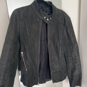 Svart skinnjacka med dragkedjor - Snygg svart skinnjacka från Vittorio med coola detaljer som dragkedjor på fickorna och hög krage med tryckknappar. Skinnjackan är inköpt i Frankrike, second hand. Äkta läder. Storlek L men sitter mer som en xs/s