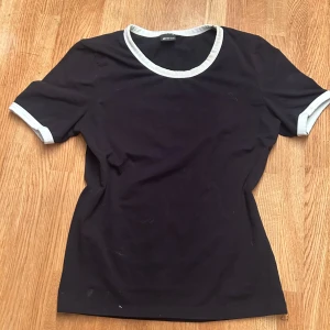 Svart t-shirt med vita detaljer Gina Tricot - Svart t-shirt från Gina Tricot i storlek S med vita kontrastkanter vid halsringning och ärmslut. Klassisk rund hals och korta ärmar❤️