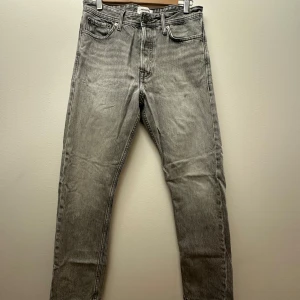 Grå loose fit jeans Jack & Jones - Snygga grå jeans från Jack & Jones i loose fit-modell, modellnamn Chris. Jeansen har raka ben, klassiska bakfickor och är tillverkade i mjukt denim. Perfekta för dig som gillar en avslappnad och trendig look. Storlek 28/32. Bra skick. Liten defekt på vänster ben se sista bilden.