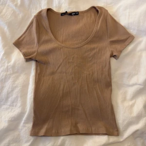 Beige ribbad topp med rund hals - Säljer en beige ribbad topp från 157 med korta ärmar och rund, djup ringning. Toppen är i mjuk bomull och har en slim passform som sitter snyggt på kroppen. Perfekt att styla med jeans eller kjol för en enkel och trendig look.