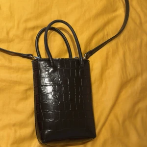 Svart axelväska i croco-imitation - Snygg svart axelväska med croco-mönstrad yta och både handtag och lång axelrem. Stilren och kompakt modell som rymmer det viktigaste. Perfekt accessoar för att lyfta din outfit.