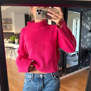 Rosa stickad polotröja med ribbad detalj - Säljer en snygg rosa stickad polotröja med ribbad struktur framtill och på kragen. Tröjan har en croppad passform, långa ärmar och en hög hals som ger en cool vibe. Perfekt att matcha med jeans för en trendig look.