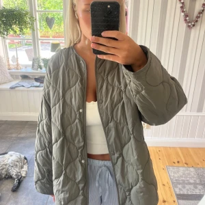 Olivgrön quiltad pufferjacka - Säljer en oversized olivgrön pufferjacka med quiltat mönster. Jackan har tryckknappar framtill, rund halsringning och långa ärmar. Perfekt för höst och vår när du vill ha en chill och trendig look.