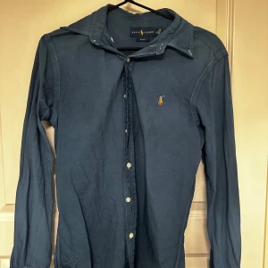 Blå skjorta Ralph Lauren - Klassisk blå skjorta från Ralph Lauren med lång ärm och knappar framtill. Skjortan har broderad logga på bröstet och en snygg krage. Perfekt för dig som gillar stilrena och tidlösa plagg.