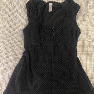 Svart ärmlös topp med knappar - Storlek M, kan bäras även om man har mindre storlek då toppen ändå följer kroppen.