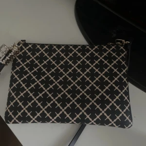 By malene birger väska - Snygg kuvertväska i svart och beige med ett rutigt grafiskt mönster. Väskan har en smidig dragkedja . Perfekt för att bära dina essentials och ge din outfit en cool touch.