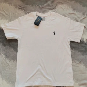 Vit Ralph Lauren T-Shirt - Helt ny - Helt ny Ralph Lauren T-shirt, helt ny, oanvänd, med prislappen kvar i storlek M! | Skick: 10 / 10 | Nypris: ~1000 | Vårt pris: 549 | Storlek: M | Tveka inte att höra av er med funderingar!