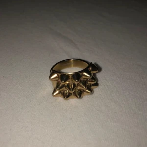 Guldig Edblad ring med nitar - Cool ring från Edblad i guldtonad metall med flera utstickande nitar runt hela ringen. Perfekt för dig som vill ha en edgy och unik accessoar som sticker ut och ger attityd till din stil.