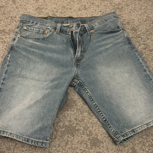 Levi's ljusblå jeansshorts 405 - Säljer ett par klassiska ljusblå jeansshorts från Levi's modell 405. De har fem fickor, gylf med dragkedja och knapp, samt den ikoniska Levi's-lappen bak. Perfekt längd och loose fit för chill stil. Passar dig som gillar vintage denim och snygga detaljer.